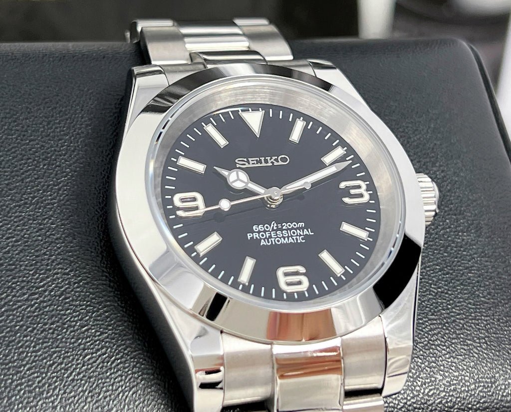 full shot of explorer style black dial Seiko mod watch with smooth bezel and stainless steel oyster bracelet