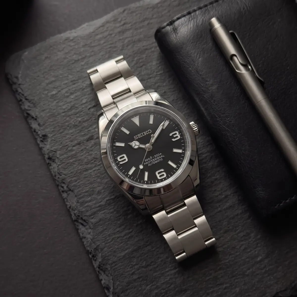 Seiko Mod Uhr DATE MOD | Stahl, schwarzes Zifferblatt mit 3-6-9-Anzeige – Automatik – Flatlay auf Schiefer – MedoMods